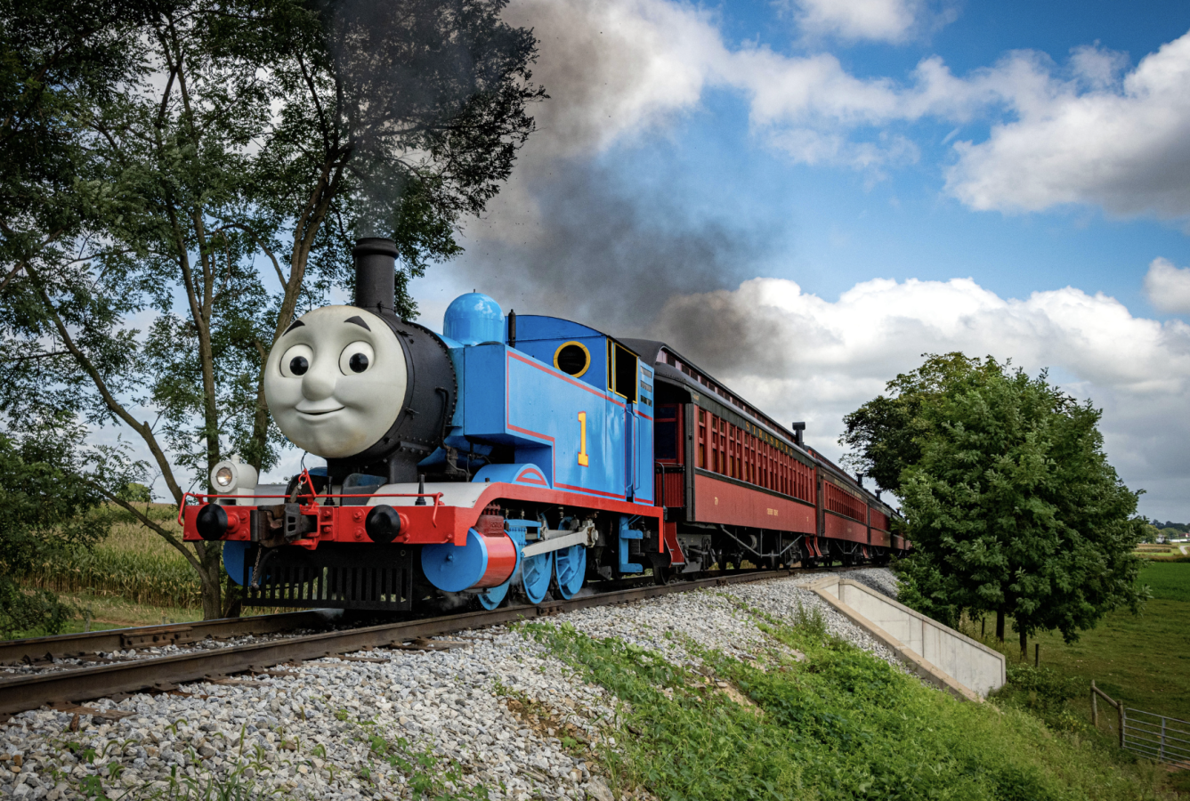 A train engine painted as the cartoon Thomas the Tank Engine pulls train cars along the Strasburg Rail Road.